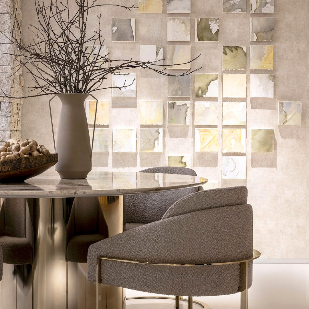 Modern dinner table surrounded by beautiful grey chairs with golden details. Ceramic vase as centerpiece. Beige walls with small square canvas paitings in neutral tones.