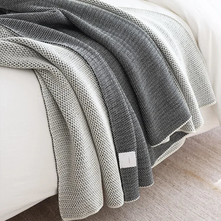 Cosy American knitted throw blanket draped over a grey sofa near a fireplace for ultimate comfort and warmth.