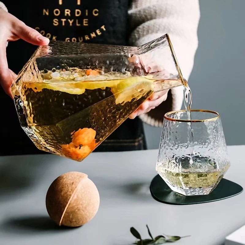 A person holding a Nordic glass pitcher filled with water and lemon slices, pouring its contents into a cup