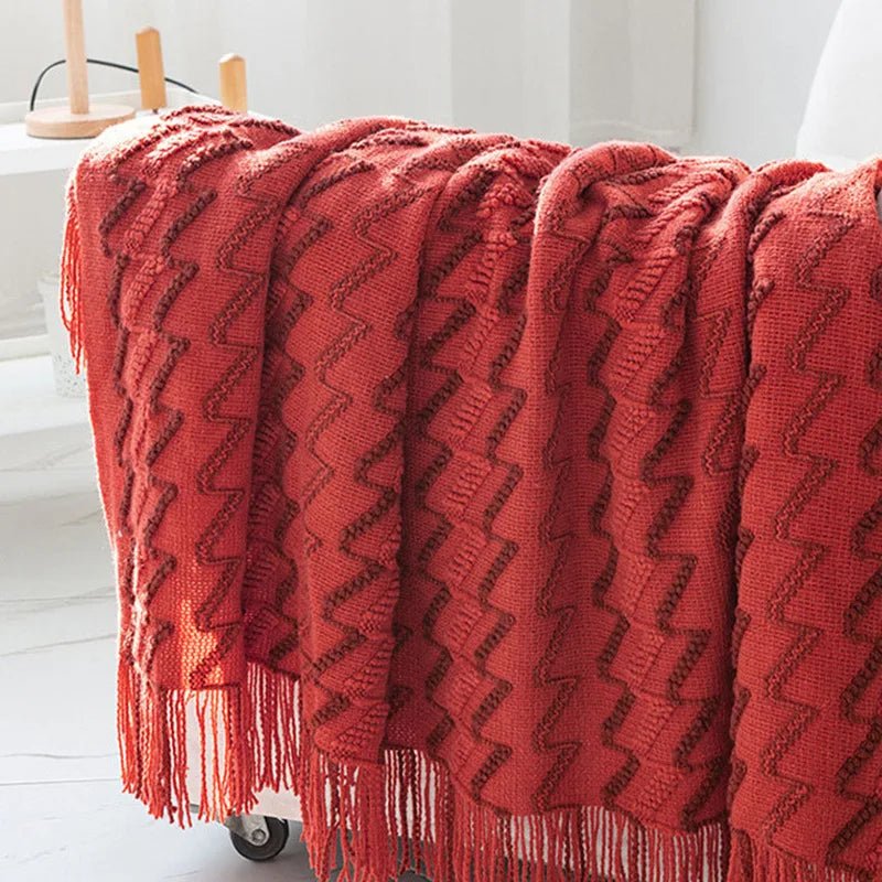 A red luxurious soft acrylic blanket draped over a couch, showcasing its soft and cozy texture.